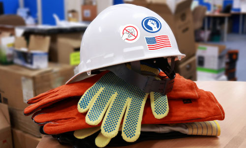 Hard Hat with 3 Stickers on it sitting on a pile of work gloves