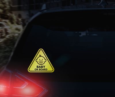 Triangle reflective sticker that says Baby On Board on the back of a black SUV in the dark.