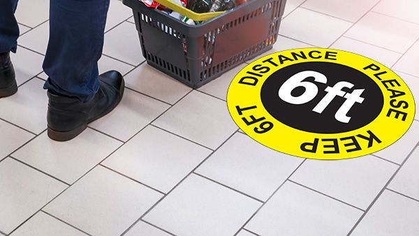 Yellow custom Floor Decal indicating social distancing on a tile grocery store floor.