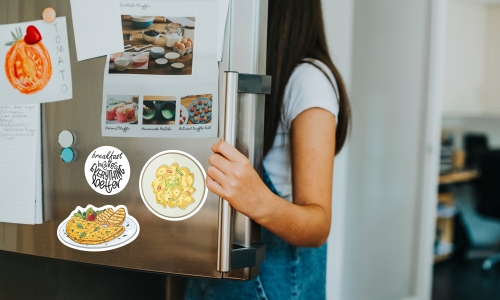 Young brunette girl digging in fridge. Fridge door has decal of an omelet and scrambled eggs