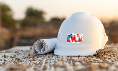 White hard hat next to rolled up construction plans with an American Flag on it