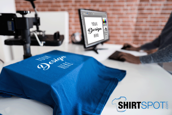 Blue custom t-shirt with computer monitor in the background. Shirtspot logo in lower right corner.