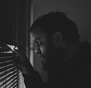 man looking outside through closed blinds