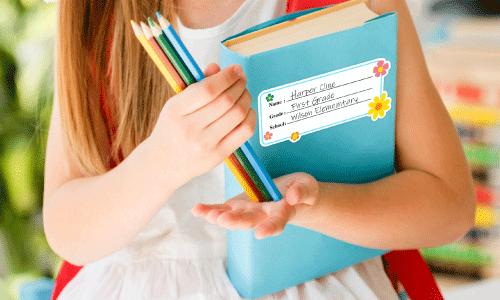 Brunette little girl holding teal school book and assortment of colored pencils with a book sticker 