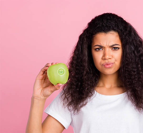 woman holding a green apple that has a sticker on it