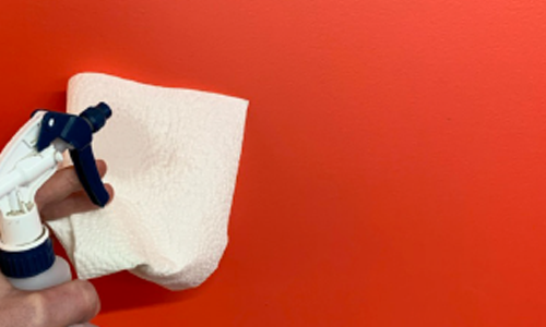 Red wall. Human male hand holding black and white spray bottle using white paper towel to clean the surface for sticker install.