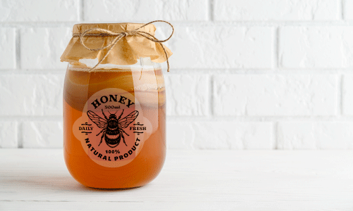 Clear honey jar label sitting on counter with white brick background