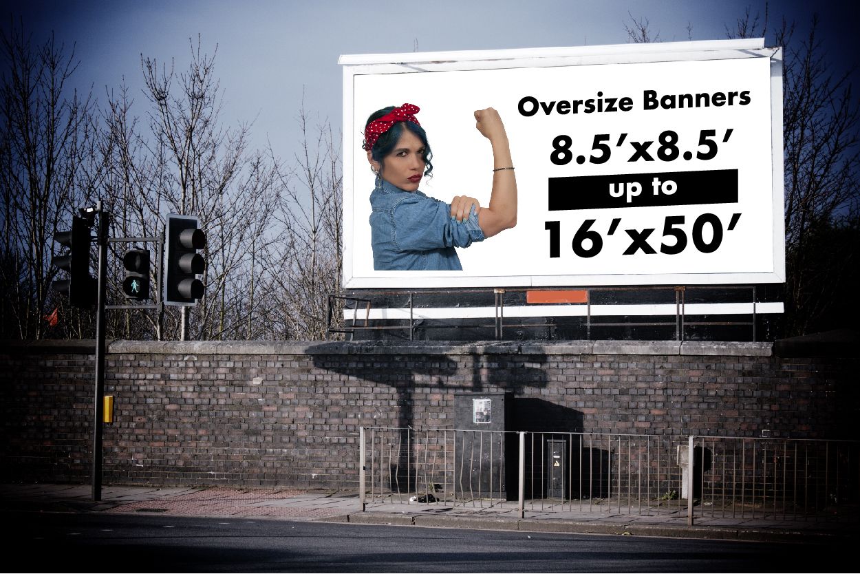 Oversized vinyl banner in white hanging at an intersection. The banner features a Rosie the Riveter graphic on the left half. To the right the text reads Oversized Banners and lists the printing sizes margins.